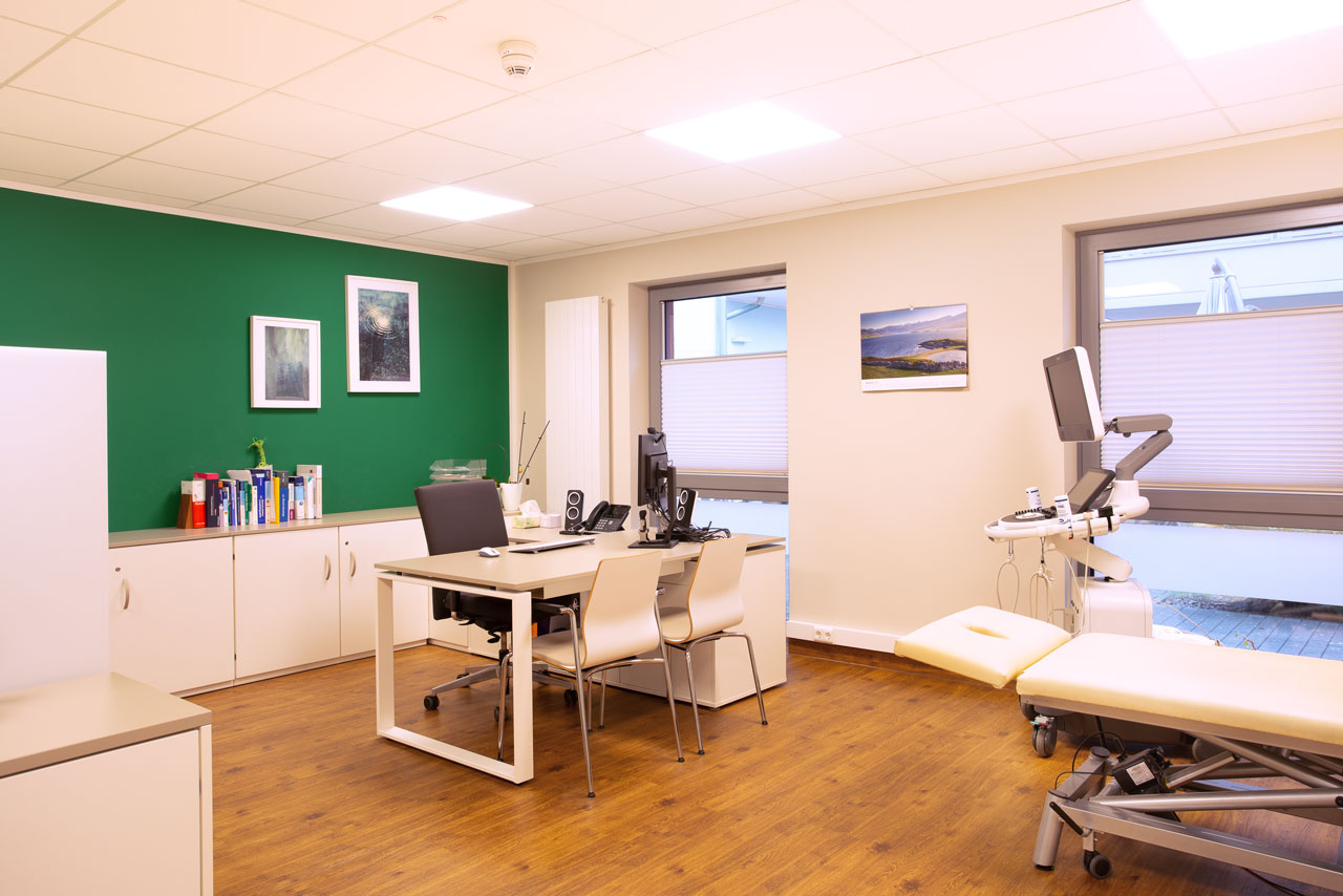 Großes Sprechzimmer mit Schreibtisch, Computer, Stühlen und Behandlungsliege