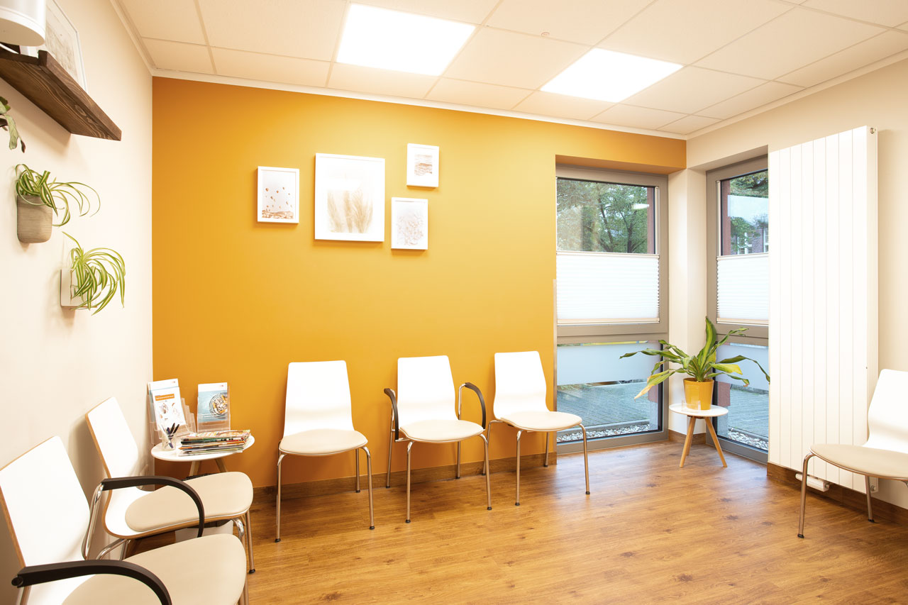 Warteraum mit Stühlen, Pflanzen und einer orangenen Wand